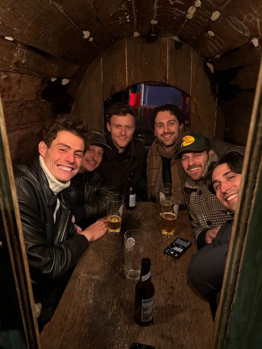 All six founders squeezed into the barrel booth around a wooden table, smiling.